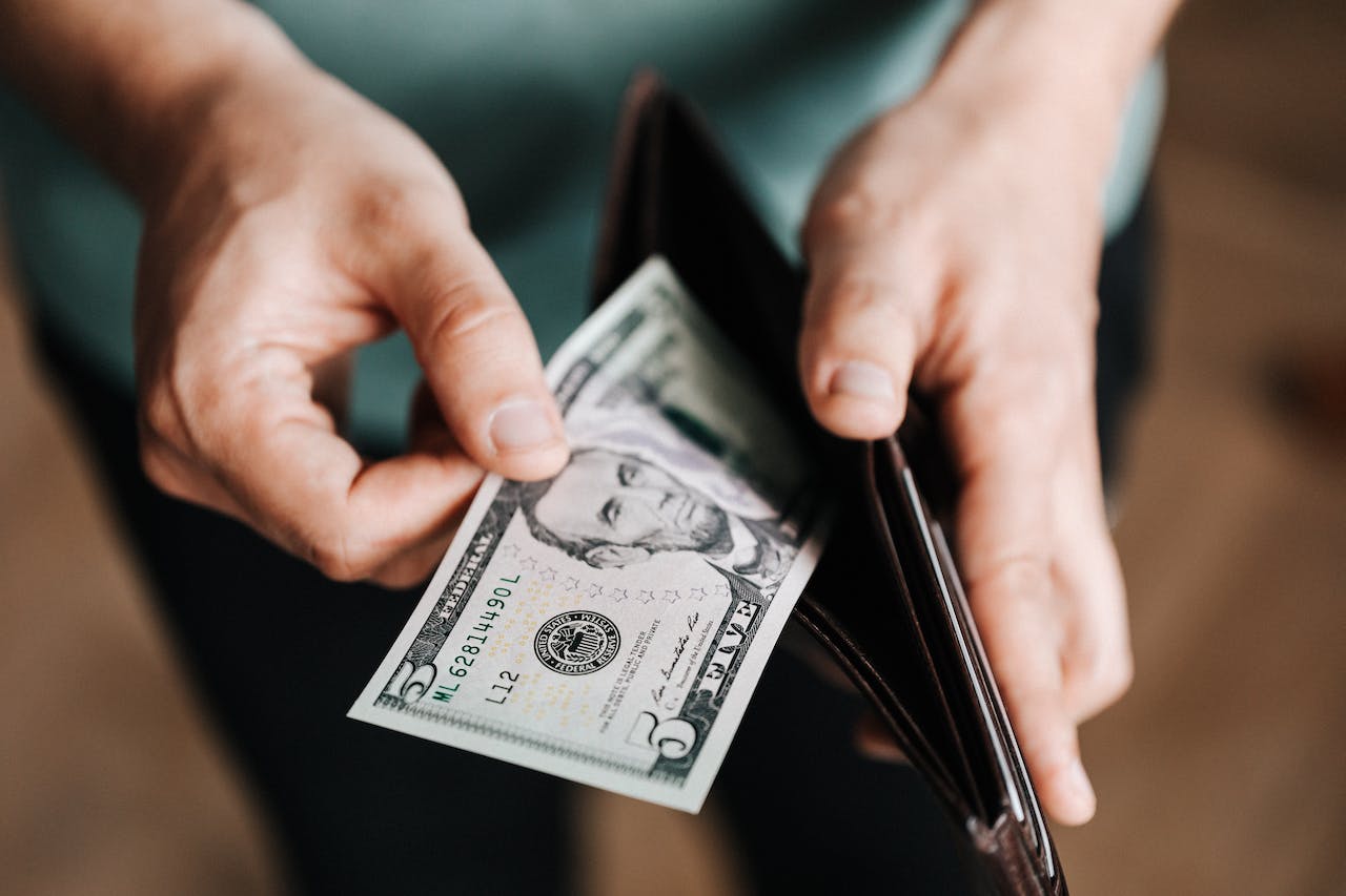 Eine Person hält ein Portemonnaie und entnimmt einen 5-Dollar-Schein, was das Konzept von Ausgaben oder der persönlichen Finanzverwaltung darstellt.