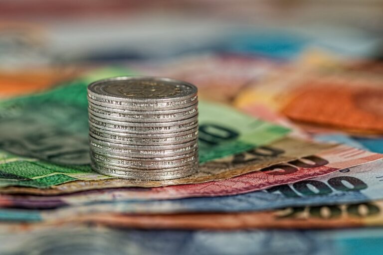 Ein Stapel von Münzen auf einem Hintergrund verschiedenfarbiger Banknoten symbolisiert finanzielle Investitionen und die bevorstehende Preissteigerung.