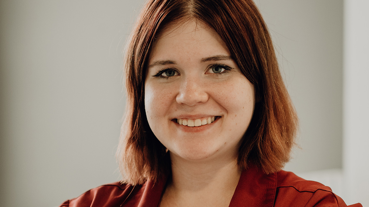 Porträt von Anastasia Giss, mit einem freundlichen Lächeln, roten Haaren und einem burgunderroten Oberteil, die eine Ausbildung zur Fachinformatikerin bei fomedia GmbH absolviert.