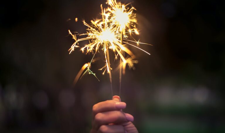 Eine Hand hält zwei leuchtende Wunderkerzen, die im Dunkeln funkeln, ein Symbol für festliche Feierlichkeiten und den Ausklang des Jahres bei der fomedia GmbH.